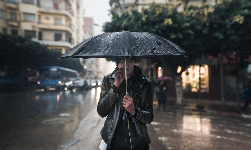 Man in leather jacket stood under an umbrella in the rain