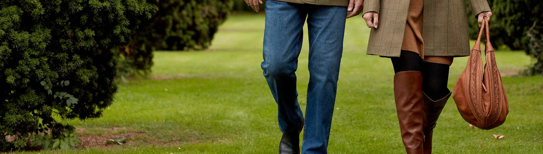 Close Up of Couples legs walking through gardens whilst holding a brown leather handbag