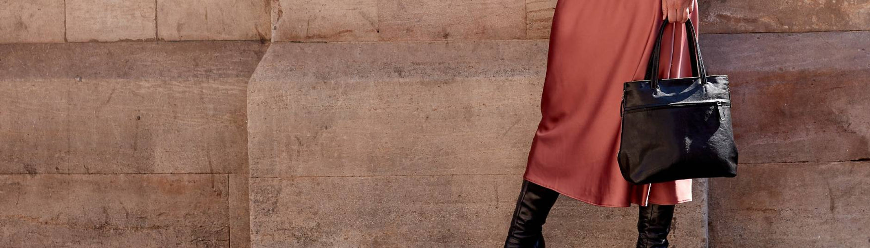 Black Leather Tote Bag being held in front of a pink silk skirt